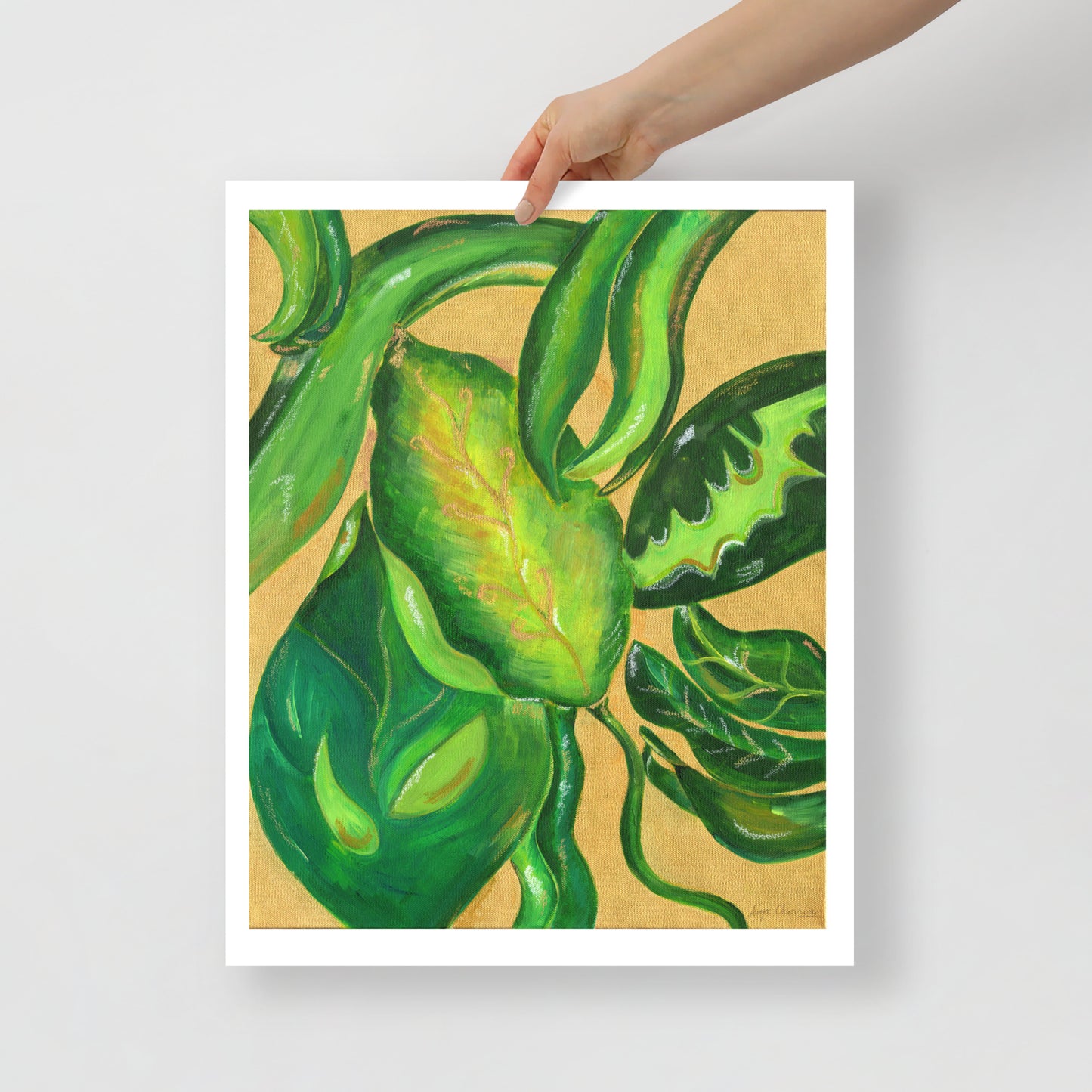 Framed artwork of green leaves held by a hand on a light gray background